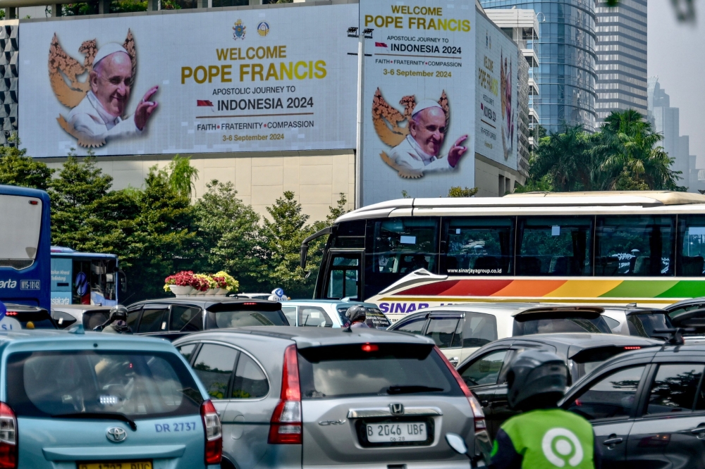 People drive their vehicles past giant billboards displaying a welcome message for Pope Francis at the business district in Jakarta. — AFP