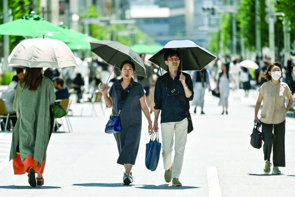 Pedestrians shelter from the sun as the summer heat returns across the country, in the Ginza area of Tokyo. — AFP file photo