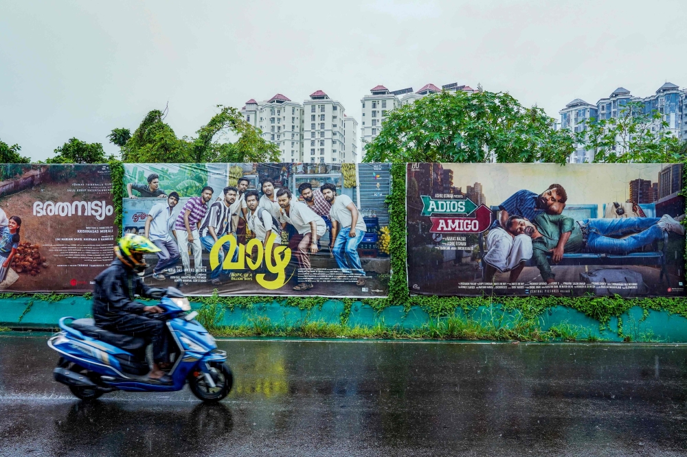 A man rides past posters of regional movies from India's Kerala-based Mollywood film industry