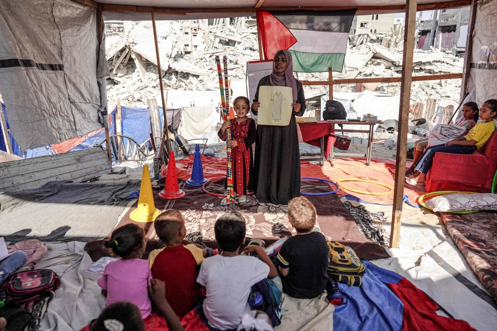 Children attend a class given by Palestinian teacher Israa Abu Mustafa at a tent amidst the rubble of collapsed buildings in Khan Yunis in the southern Gaza Strip. - AFP

