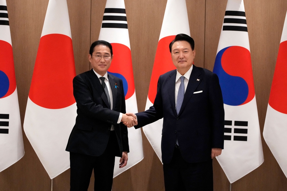 South Korea's President Yoon Suk Yeol (R) and Japan's Prime Minister Fumio Kishida shake hands  