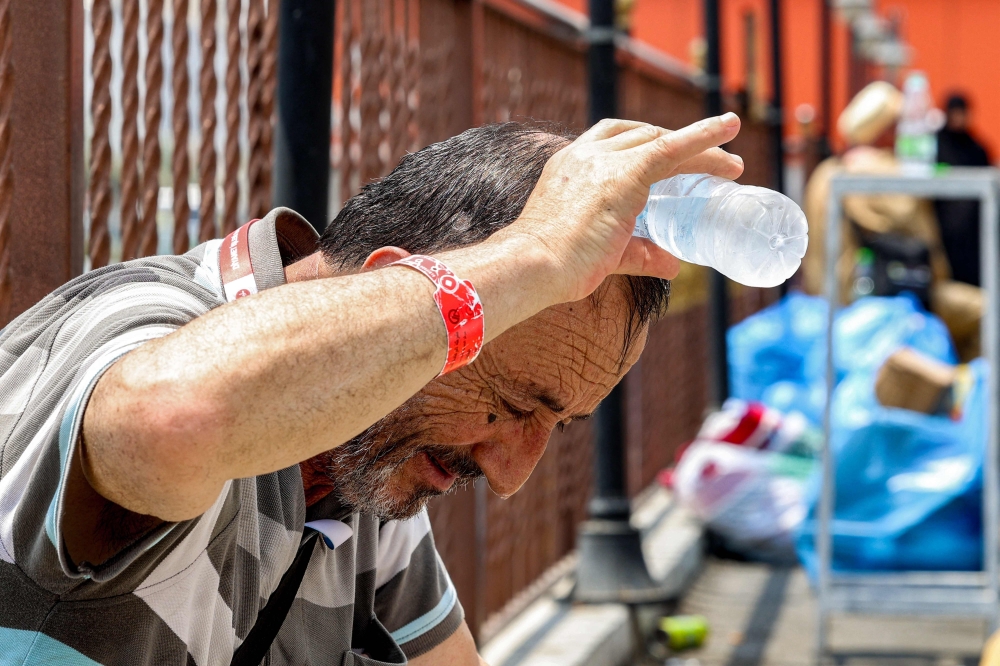 A Turkish pilgrim pours cold water from a bottle on his head to cool off as he waits in Mecca 