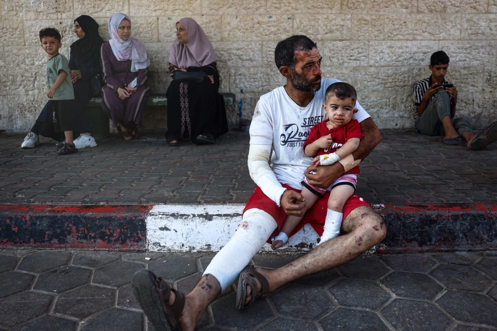 Palestinian man and his son, both injured in an Israeli bombing in the Bureij refugee camp, sit outside the Al-Aqsa Martyrs Hospital in Deir al-Balah. — AFP 