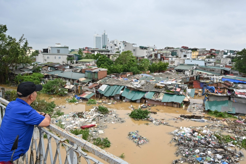 A man standing on Long Bien Bridge looks down at houses partially submerged in floodwaters in Hanoi. — AFP 