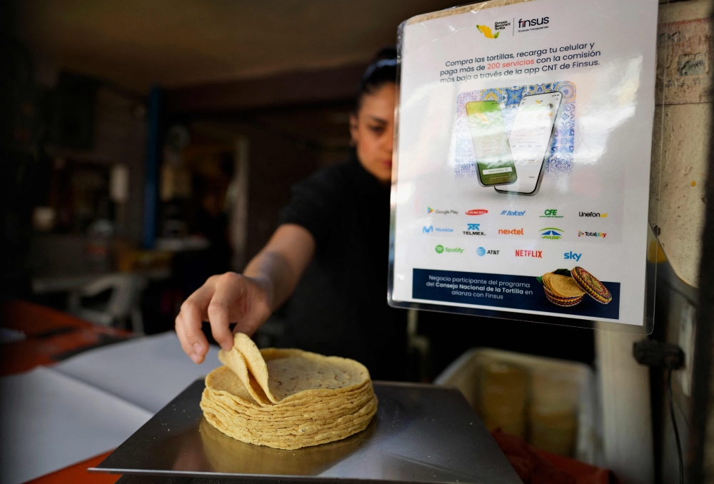 A worker weighs tortillas next to a sign with information about an app to buy tortillas at a tortilla factory in Mexico City