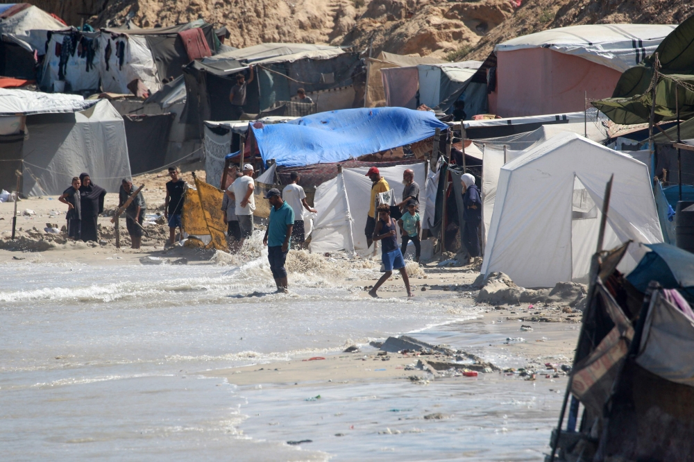 Displaced Palestinians gather near tents that were flooded with sea water, along the shore of Khan Yunis in the southern Gaza Strip. — AFP 