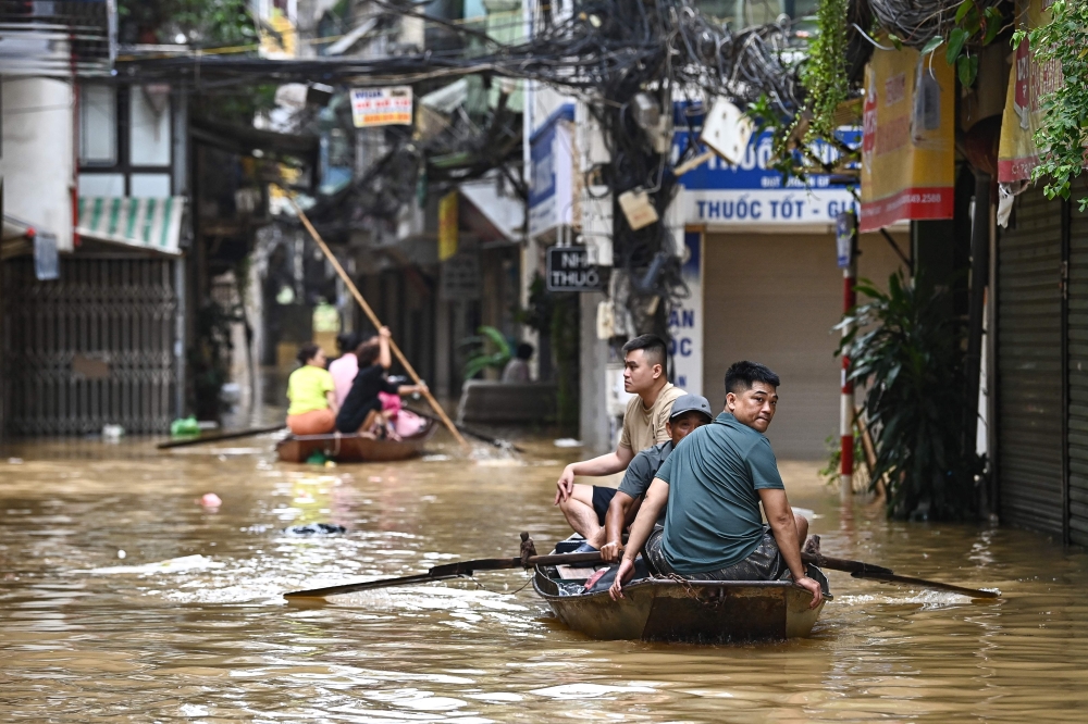 People wade through flood waters on a boat in Hanoi. — AFP file photo