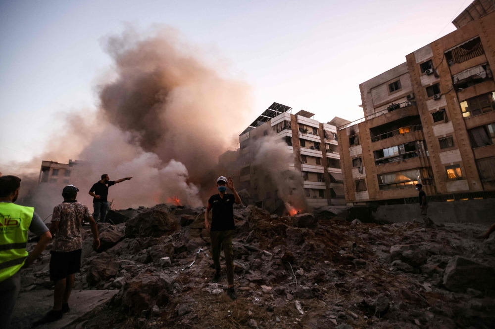 People and rescuers stand amid the rubble of a building destroyed in an Israeli air strike in the Haret Hreik  