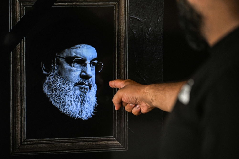 A man points to a television set displaying an image of the late leader of Hezbollah Hassan Nasrallah with a black stripe for mourning during a broadcast from the private Lebanese station NBN in Beirut on September 28, 2024. Lebanon's Iran-backed Hezbollah group confirmed on September 28, 2024 that its leader Hassan Nasrallah had been killed, after Israel said it had "eliminated" him in a strike on south Beirut a day earlier.