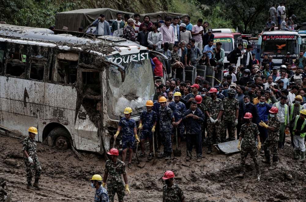 People stranded at the Tribhuwan Highway look on as rescue personnel work to retrieve the bodies of the victims from a landslide triggered by heavy rainfall in Dhading, Nepal. — Reuters 