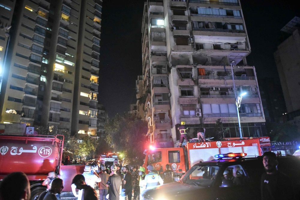 Firefighters gather at the site of an apartment building hit by an Israeli air strike in Beirut's Cola district
