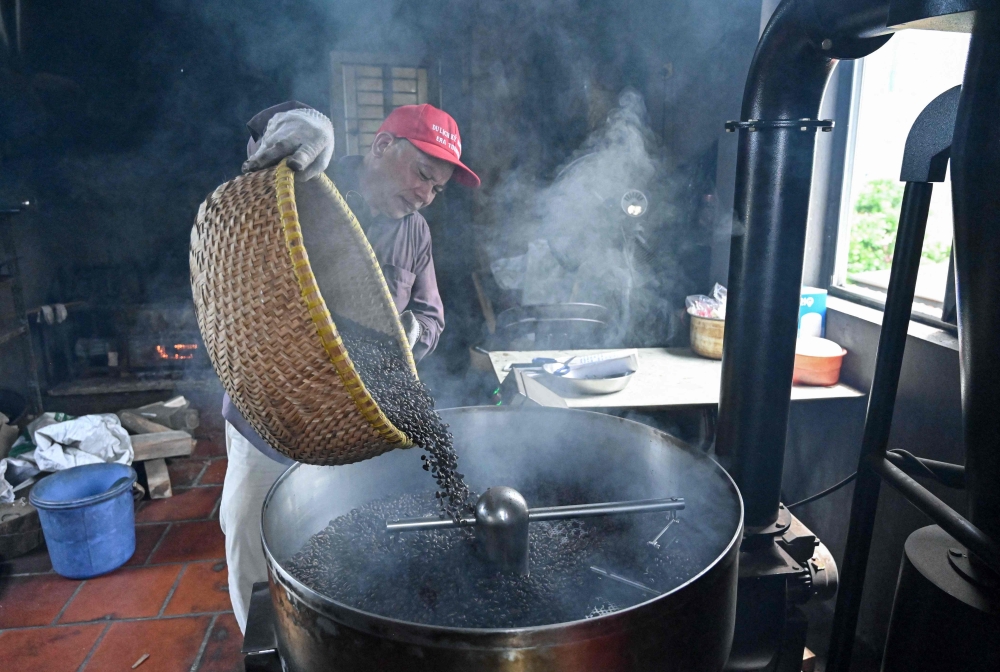 This photo taken on August 21, 2024 shows a worker roasting coffee beans at Thai Cafe's production facility in Hanoi. Traditionally taken black, sometimes with condensed milk, salt or even egg, coffee has long been an integral part of Vietnamese culture. But running a cafe is not a career that many of Vietnam's growing group of ambitious middle-class parents would choose for their children. - To go with 'VIETNAM-COFFEE-CAFE,FOCUS' by Alice Philipson and Lam Nguyen
 (Photo by Nhac NGUYEN / AFP) / To go with 'VIETNAM-COFFEE-CAFE,FOCUS' by Alice Philipson and Lam Nguyen

