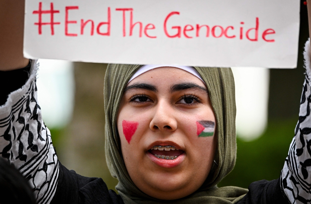 A protester holds a "End the Genocide" sign as people rally in support of Gaza and Lebanon in front of the City Hall 