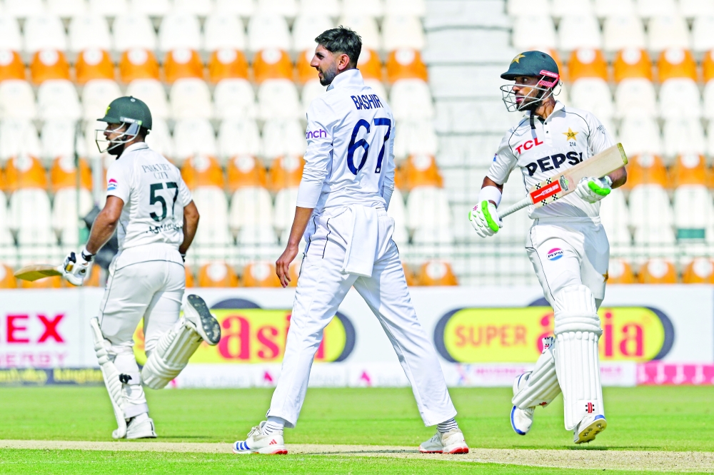 Pakistan's captain Shan Masood (R) and Abdullah Shafique (L) run between the wickets as England's Shoaib Bashir looks on during the first day of the first Test cricket match between Pakistan and England, at the Multan Cricket Stadium in Multan on October 7, 2024.