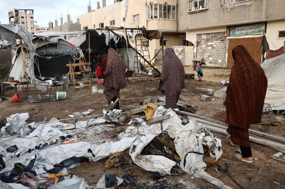 Women walk amid damaged tents following an Israeli air strike on the Bureij refugee camp. — AFP