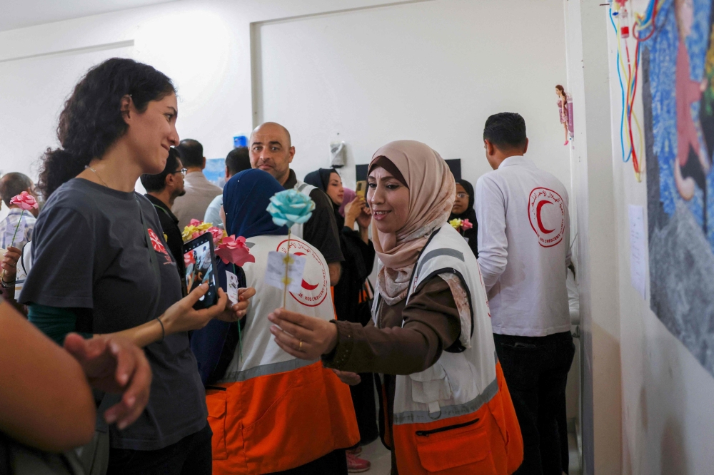 A volunteer offers flowers at an art exhibition of works by displaced Palestinian children as part of a psychological rehabilitation and support sessions, organised by the Palestinian Red Crescent, in Khan Yunis in the southern Gaza Strip on October 10, 2024.  (Photo by BASHAR TALEB / AFP)