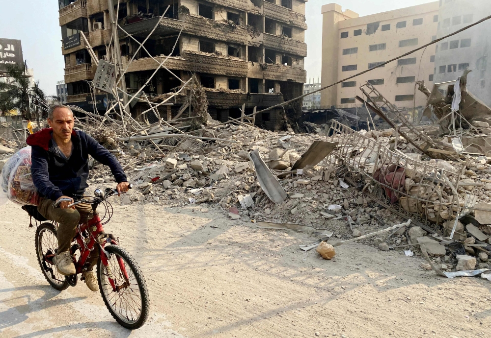 A man cycles past a destroyed building at the site of an overnight Israeli airstrikes that targeted a Beirut's southern suburb. - AFP
