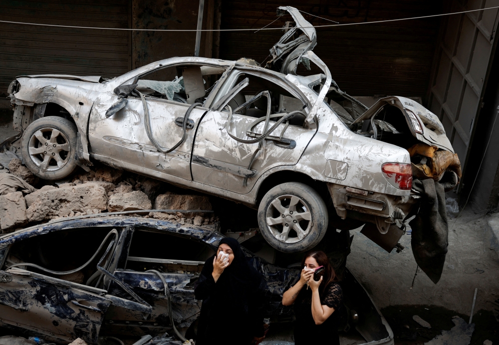Women stand next to damaged vehicles at the site of an Israeli air strike, amid ongoing hostilities in Beirut  