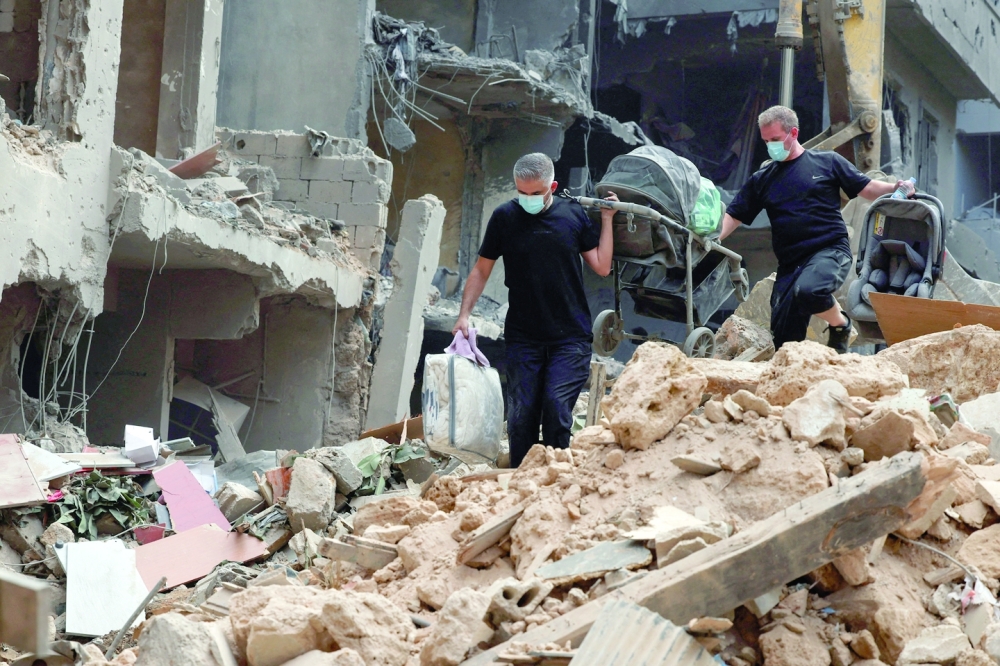 People carry belongings as they walk on rubble at the site of an Israeli strike, in Beirut. — Reuters