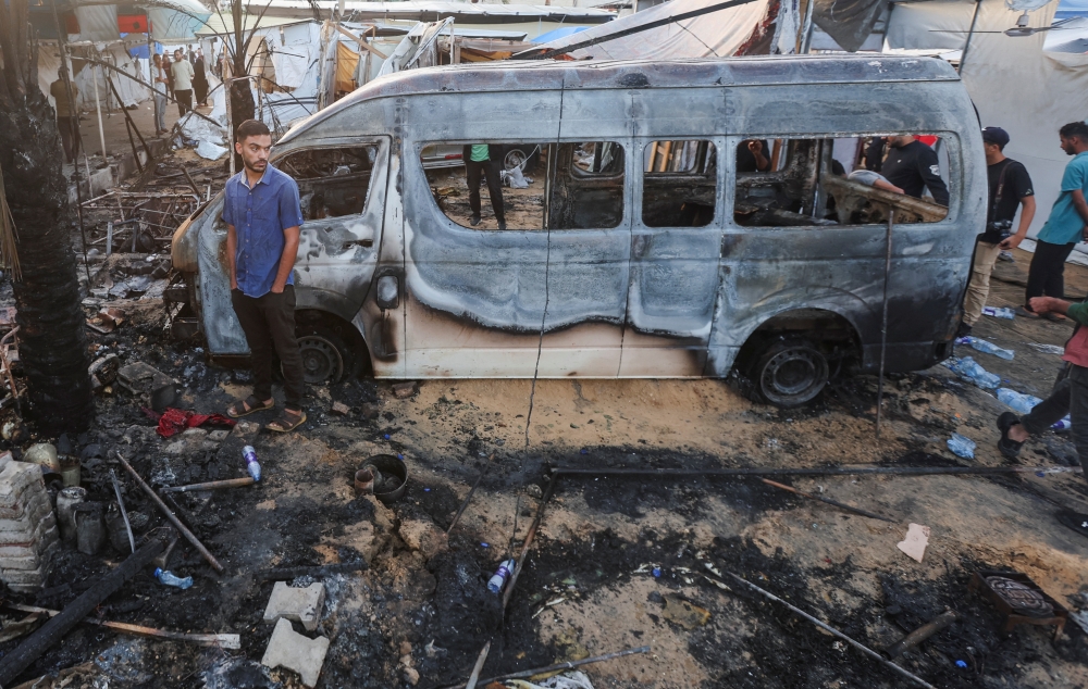 A Palestinian man stands next to a destroyed vehicle at the site of an Israeli strike on tents sheltering displaced people, amid the Israel-Hamas conflict, at Al-Aqsa Martyrs hospital in Deir Al-Balah in the central Gaza Strip, October 14, 2024. REUTERS/Ramadan Abed
