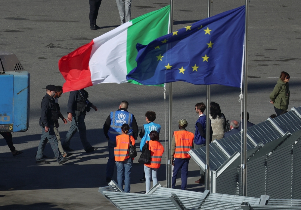 Migrants and security officials walk as they arrive in Albania, in Shengjin. — Reuters