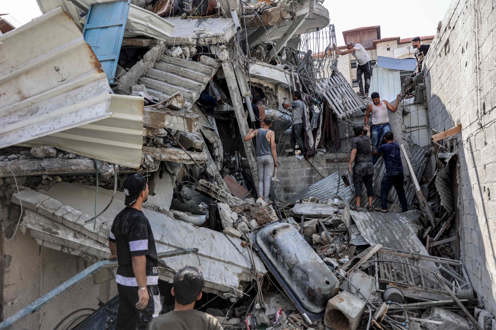 People gather outside a collapsed building as they attempt to extricate a man from underneath the rubble following Israeli bombardment in the Saftawi district 
