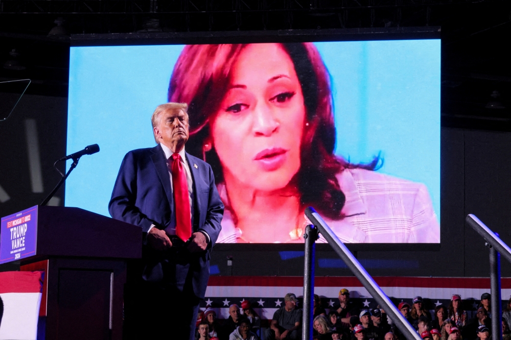Donald Trump looks on as Kamala Harris' face appears as a video plays on a screen