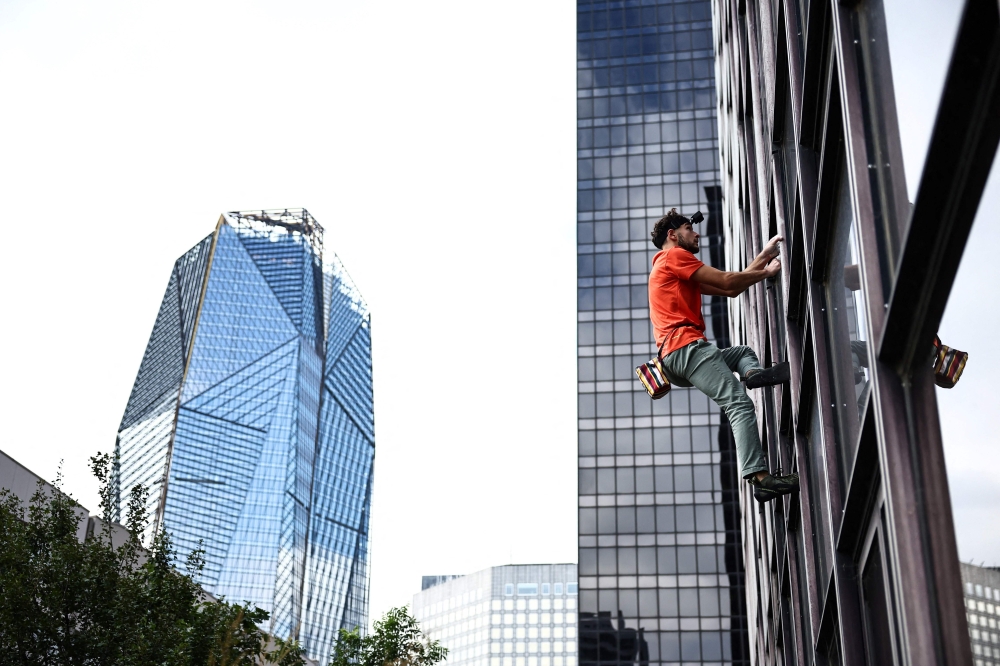 French urban climber Titouan Leduc begins climbing the Franklin Tower, a 115-metre-high office skyscraper located in La Defense business district, west of Paris, on October 3, 2024. Leduc, a 23-year-old urban climber from northeastern France, likes to scale skyscrapers without any ropes or specialist equipment, wearing only a pair of climbing boots. (Photo by Anne-Christine POUJOULAT / AFP)

