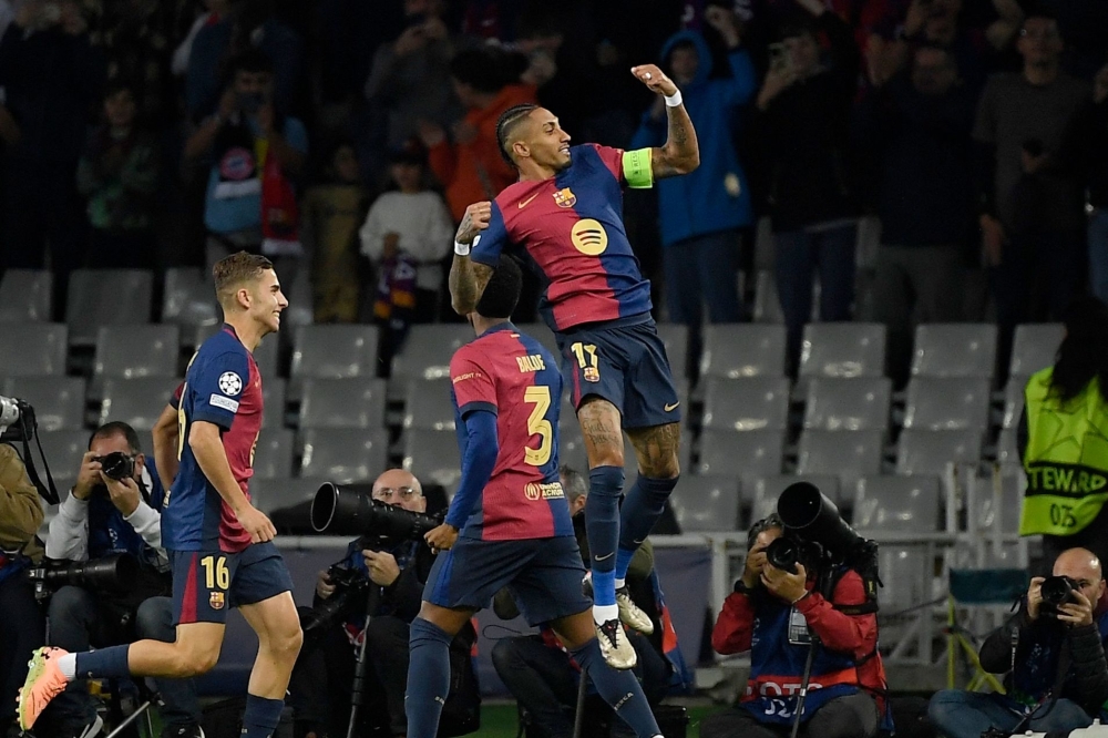 TOPSHOT - Barcelona's Brazilian forward #11 Raphinha (TOP) celebrates scoring the opening goal during the UEFA Champions League, league phase day 3 football match between FC Barcelona and FC Bayern Munich at the Estadi Olimpic Lluis Companys in Barcelona on October 23, 2024. (Photo by Josep LAGO / AFP)

