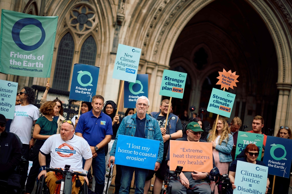 Kevin Jordan (C), holding a placard reading 'I lost my home to coastal erosion' demonstrates with environmental protestors in front of the Royal Courts of Justice 