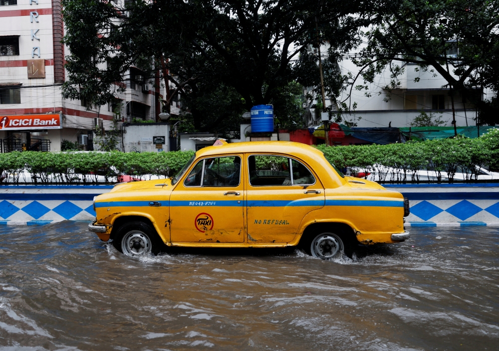 A yellow taxi passes through a water-logged road after rains caused by cyclone Dana in Kolkata 