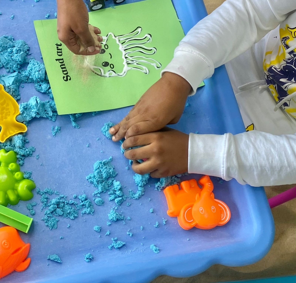 A child plays with textures (sand play and making sand art)