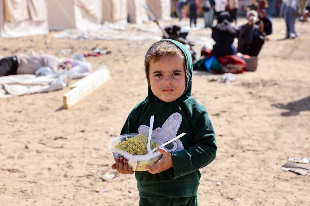 A displaced child who fled with family members Israeli army operations in the northern Gaza Strip, carries a bowl of food 