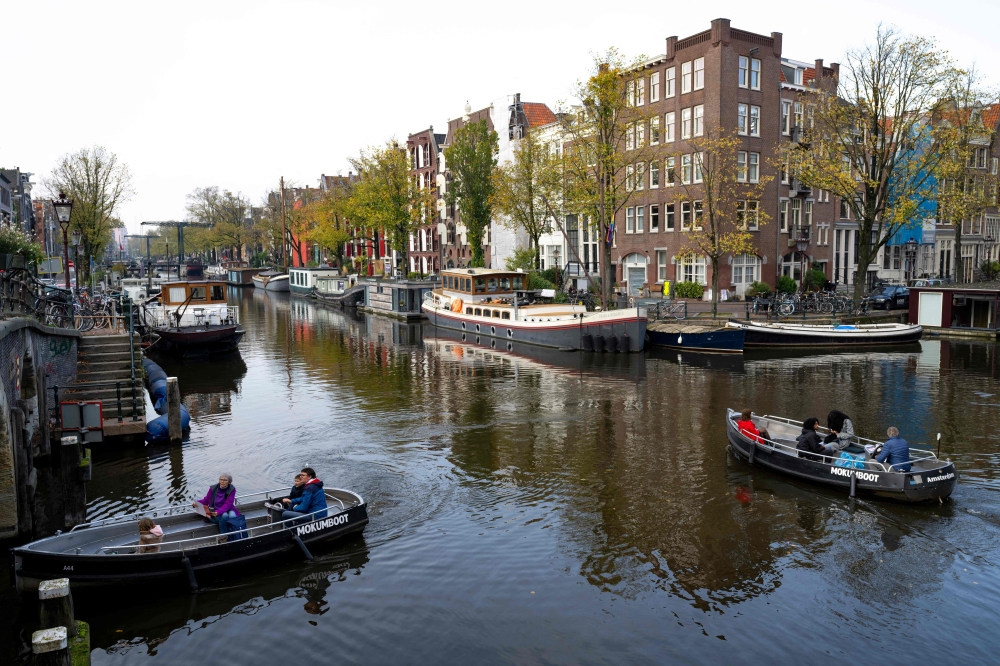 People navigate small boats on the Lekkersluis canal in Amsterdam on October 23, 2024, as the city launches its 750th anniversary celebrations. This year, De Jordaan is the subject of a musical created to celebrate the 750th anniversary of Amsterdam, for which the festivities kick off on October 27, 2024, and run for a year.
A neighbourhood known for its popular music and outspoken residents, De Jordaan crystallises the changes that have taken place in the Dutch capital, from its working-class origins to its recent gentrification. (Photo by Nick Gammon / AFP)

