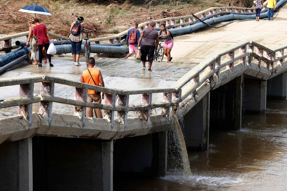 People crosses an affected bridge days after the passage of hurricane Oscar in Guantanamo, Cuba on October 29. - AFP

