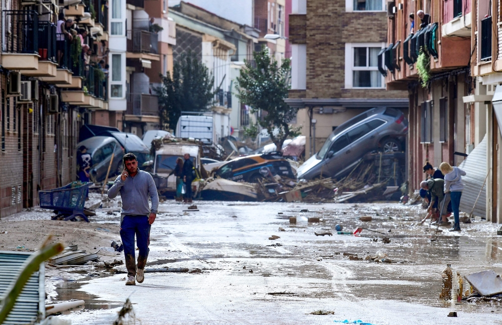 Residents are pictured next to cars piled in a street covered in mud, near Valencia. — AFP