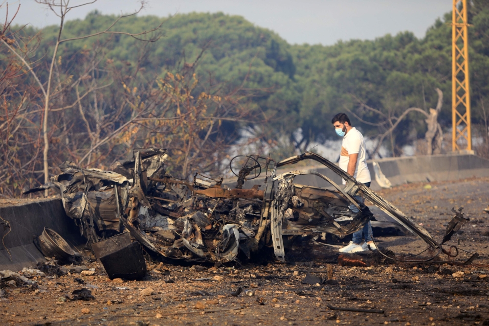 A man checks the wreckage of a vehicle on the Araya-Kahhale road, near Beirut. — AFP