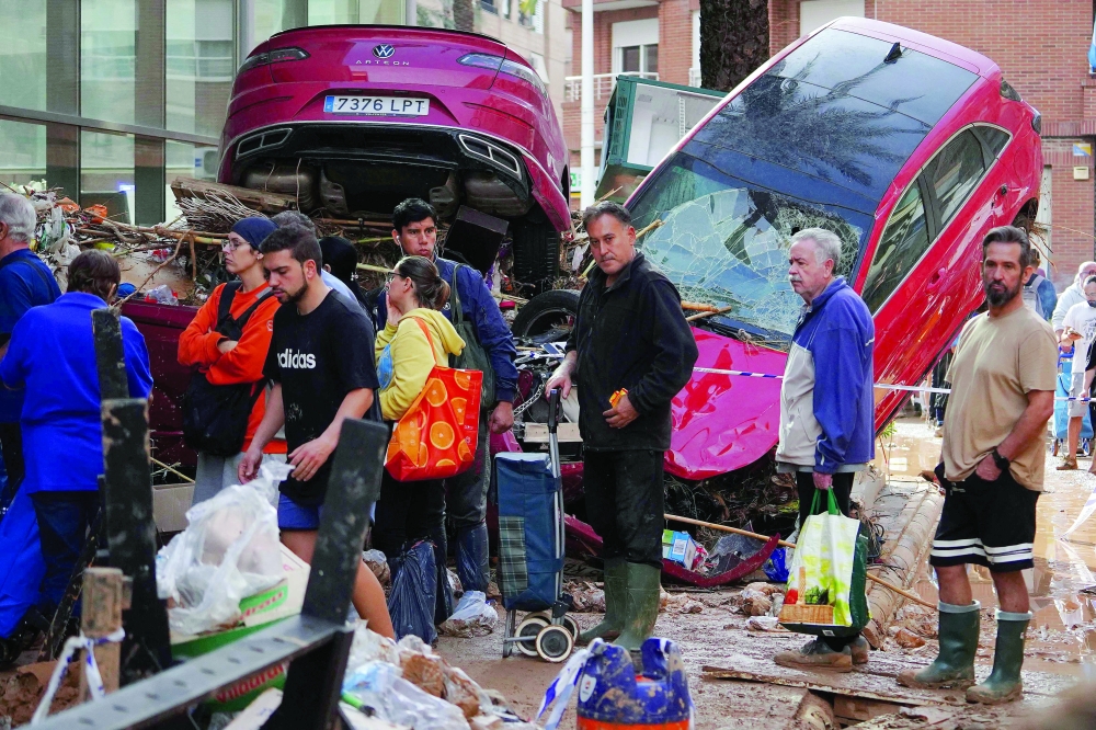 People queue for supplies close to a pile of wrecked cars following the devastating effects of flooding on the town of Paiporta, in the region of Valencia, eastern Spain. - AFP