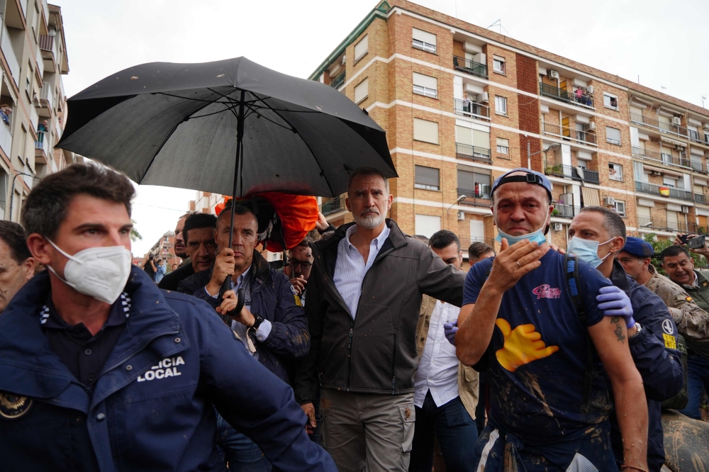 King Felipe VI of Spain is protected with an umbrella as angry residents heckle him and throw mud and objects during his visit to Paiporta, in the region of Valencia, eastern Spain, on November 3, 2024, in the aftermath of devastating deadly floods.  (Photo by Manaure Quintero / AFP)