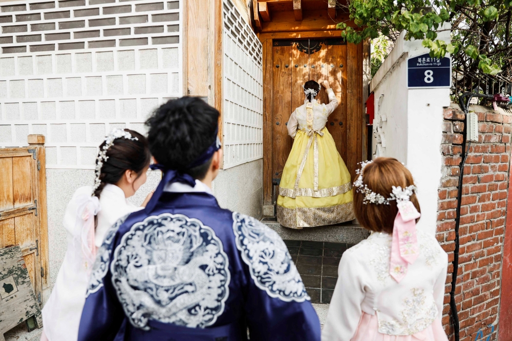 A tourist dressed in traditional Korean hanbok knocks on a door to pose for photos in front of a hanok (traditional Korean house) entrance in Bukchon Hanok Village in Seoul, South Korea, October 25, 2024. REUTERS/Kim Soo-hyeon
