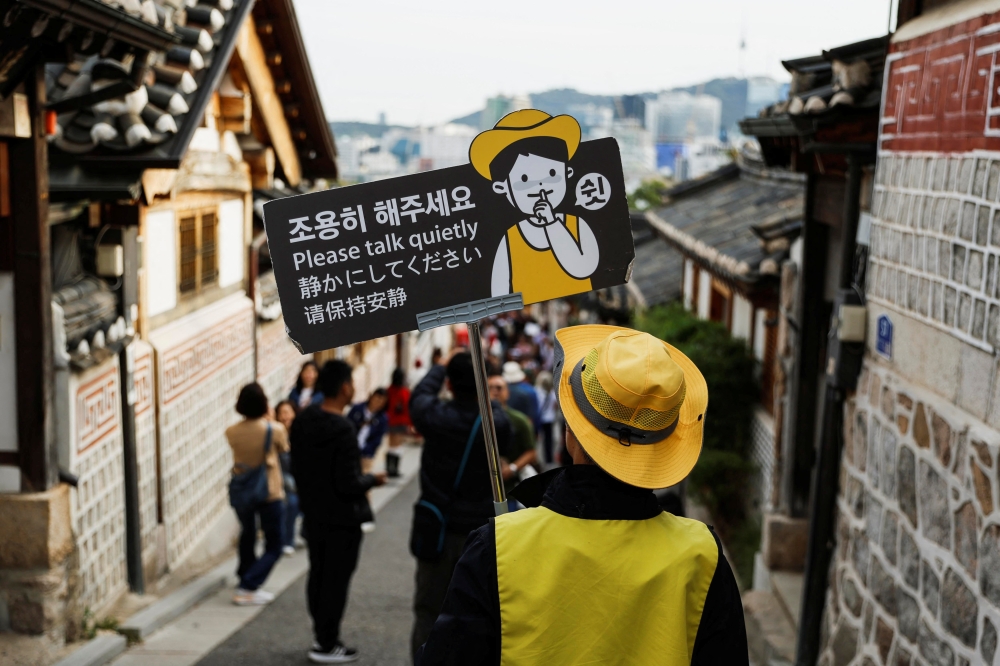 A person monitoring noise holds a sign that says 'Please talk quietly' at Bukchon Hanok Village in Seoul, South Korea, October 25, 2024. REUTERS/Kim Soo-hyeon
