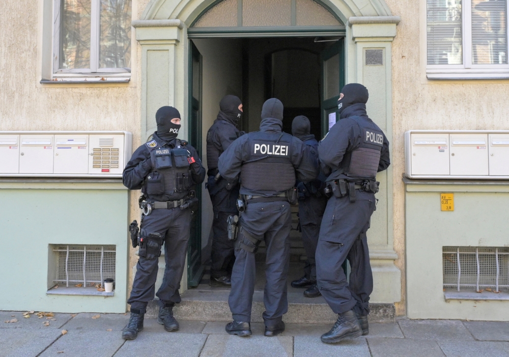 Masked police officers guard a house after having arrested suspects, in Dresden, Germany. — Reuters 