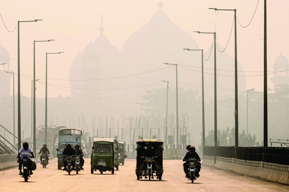 Commuters ride along a street engulfed in smog, in Lahore. — AFP