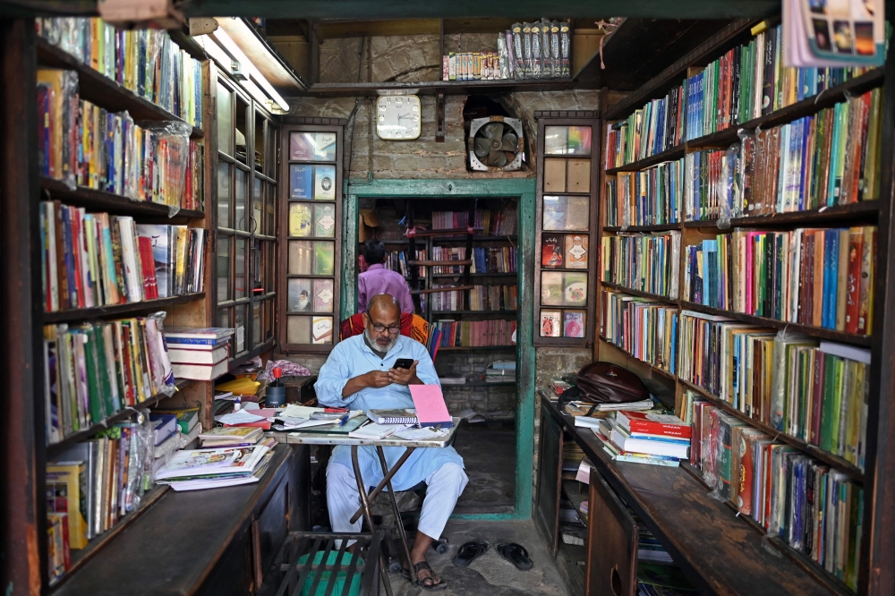 This photograph taken on October 14, 2024 shows a shopowner using his mobile phone while sitting inside his Urdu literature establishment at Urdu Bazar in the old quarters of Delhi. Urdu, spoken by many millions today, has a rich past that reflects how cultures melded to forge India's complex history. - To go with 'India-Language-History-Urdu', FOCUS by Aishwarya KUMAR and Abhaya SRIVASTAVA
 (Photo by Sajjad HUSSAIN / AFP) / To go with 'India-Language-History-Urdu', FOCUS by Aishwarya KUMAR and Abhaya SRIVASTAVA

