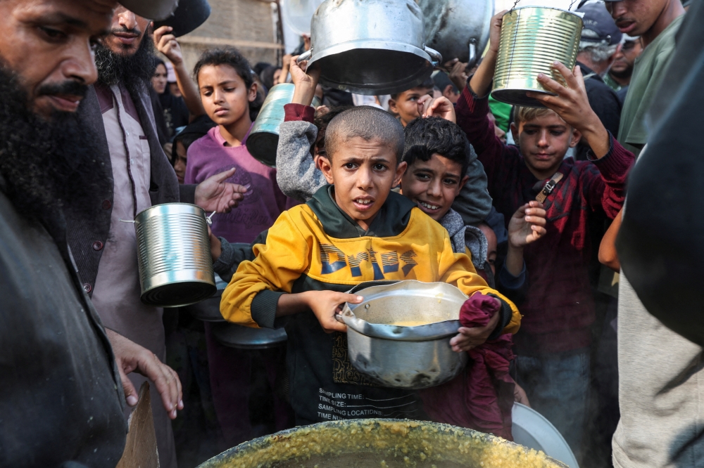 Displaced Palestinians gather to receive meals cooked by a charity kitchen, in central Gaza. — Reuters  