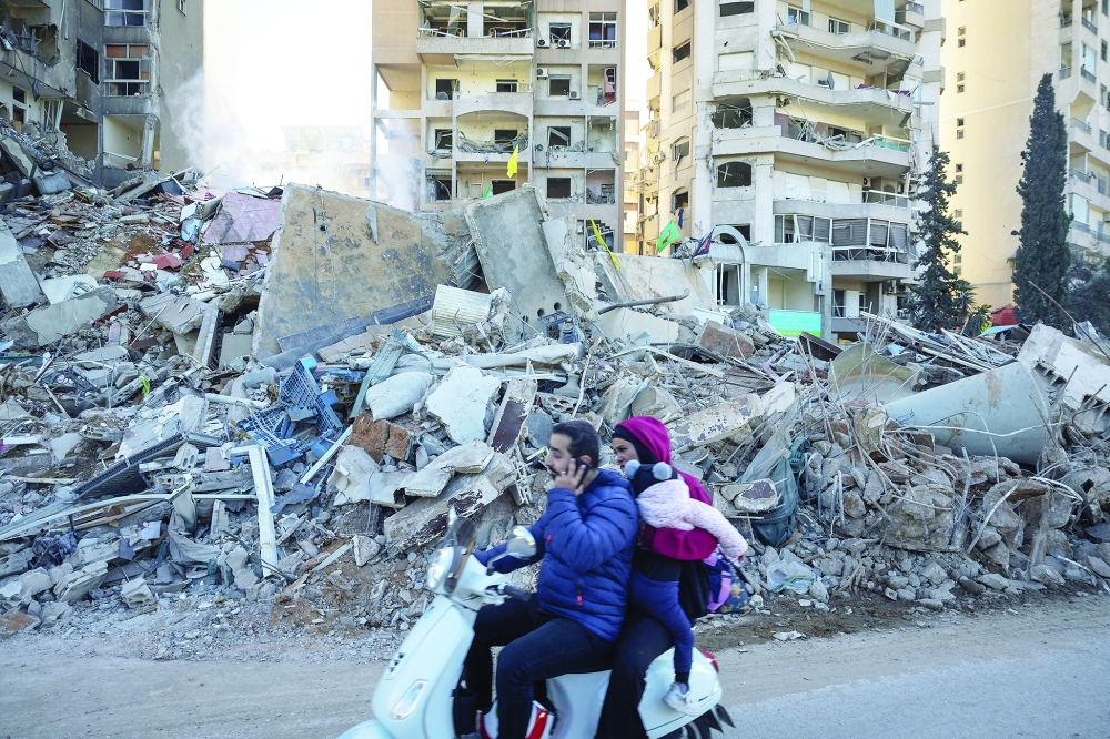 People ride on a scooter past a damaged apartment building in the aftermath of an Israeli strike in Tayouneh, Beirut. - Reuters