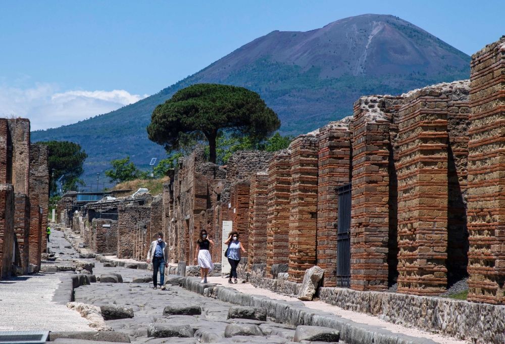 Visitors walk across the archeological site of Pompeii at the bottom of the Mount Vesuvius volcano (Rear) on May 26, 2020, as the country eases its lockdown aimed at curbing the spread of the COVID-19 infection, caused by the novel coronavirus. Daily cap of 20,000 visitors to archaeological park comes into effect today on November 15, 2024.  (Photo by Tiziana FABI / AFP)

