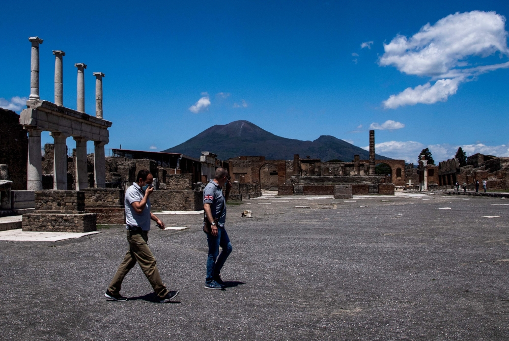 People walks across the archeological site of Pompeii at the bottom of Mount Vesuvius volcano (Rear) on May 26, 2020, as the country eases its lockdown aimed at curbing the spread of the COVID-19 infection, caused by the novel coronavirus. Daily cap of 20,000 visitors to archaeological park comes into effect today on November 15, 2024.  (Photo by Tiziana FABI / AFP)

