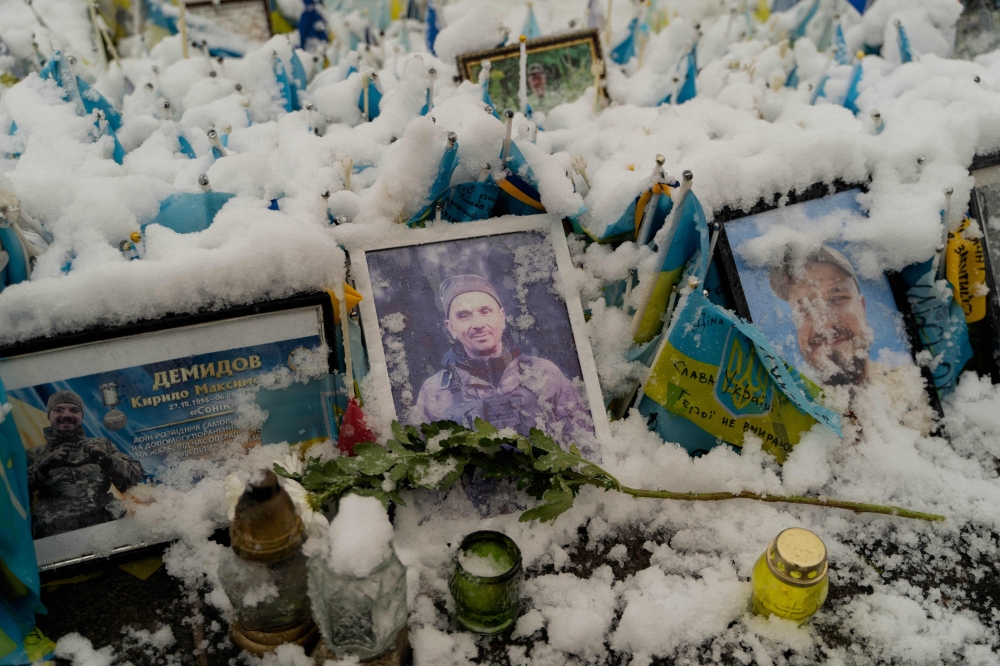 Portraits of Ukrainian military members covered in snow are seen at the makeshift memorial to Ukrainian and foreign fighters