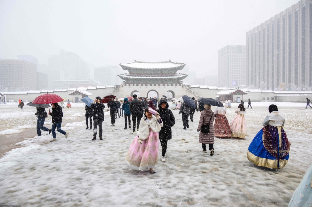 Visitors wearing traditional hanbok dresses are seen on the grounds of Gyeongbokgung Palace amid heavy snowfall in central Seoul. — AFP